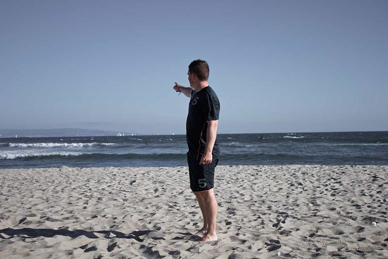 Félix Ossa - Dónde está Colombia? - Imagen de un hombre en la playa apuntando su hacia atrás